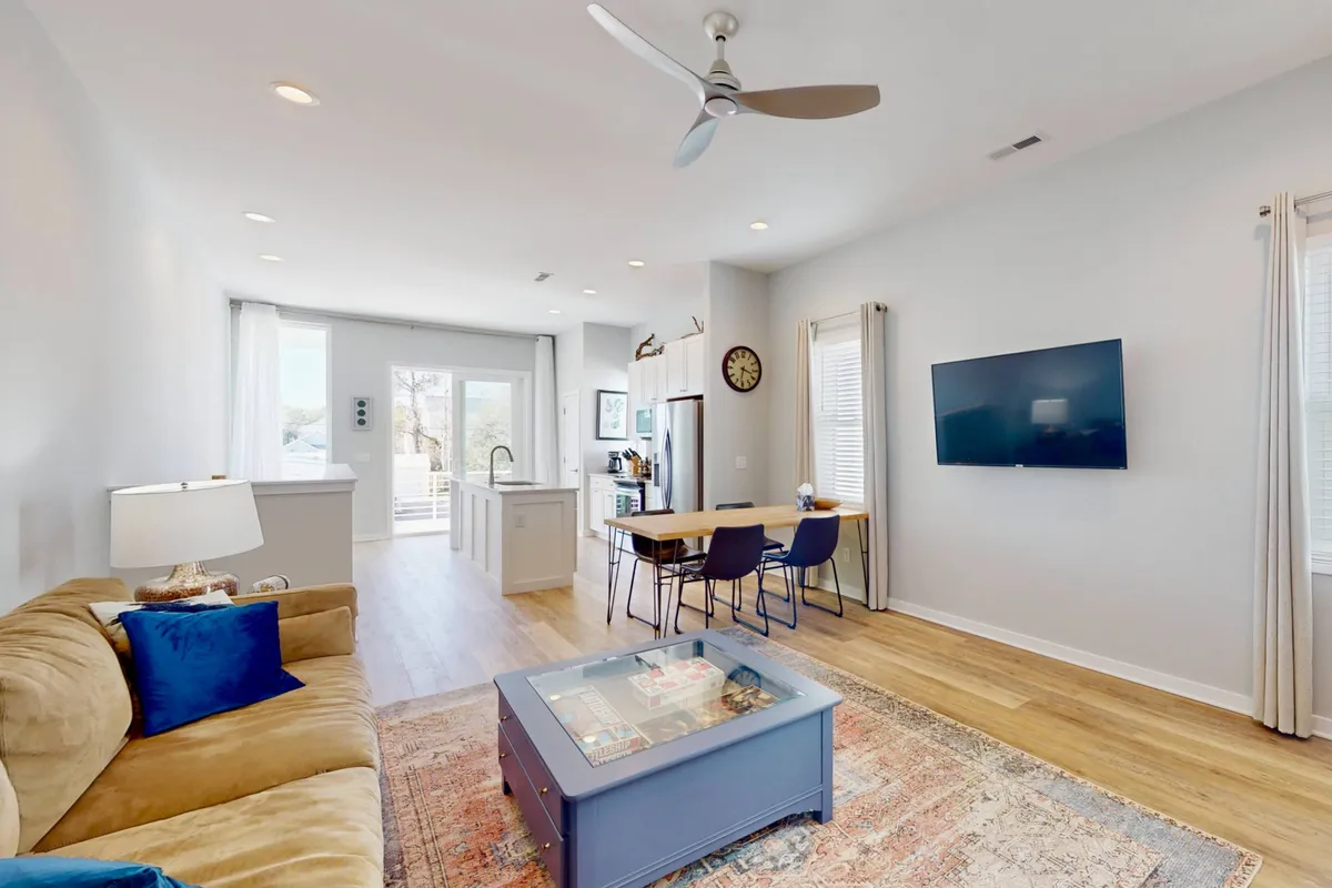 An open-concept living area that seamlessly integrates the sofa, coffee table, kitchen island, dining area, and television. The space is filled with natural light and features inviting furnishings, offering a direct view of both the lounging and dining areas as well as the modern kitchen.