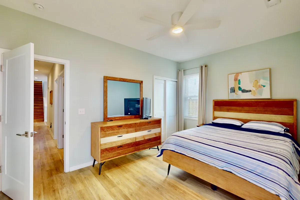 A bright and comfortable bedroom with a queen bed, a dresser, and a window admitting natural light. The room is styled with simple decorations and artwork, creating a cozy refuge for guests.