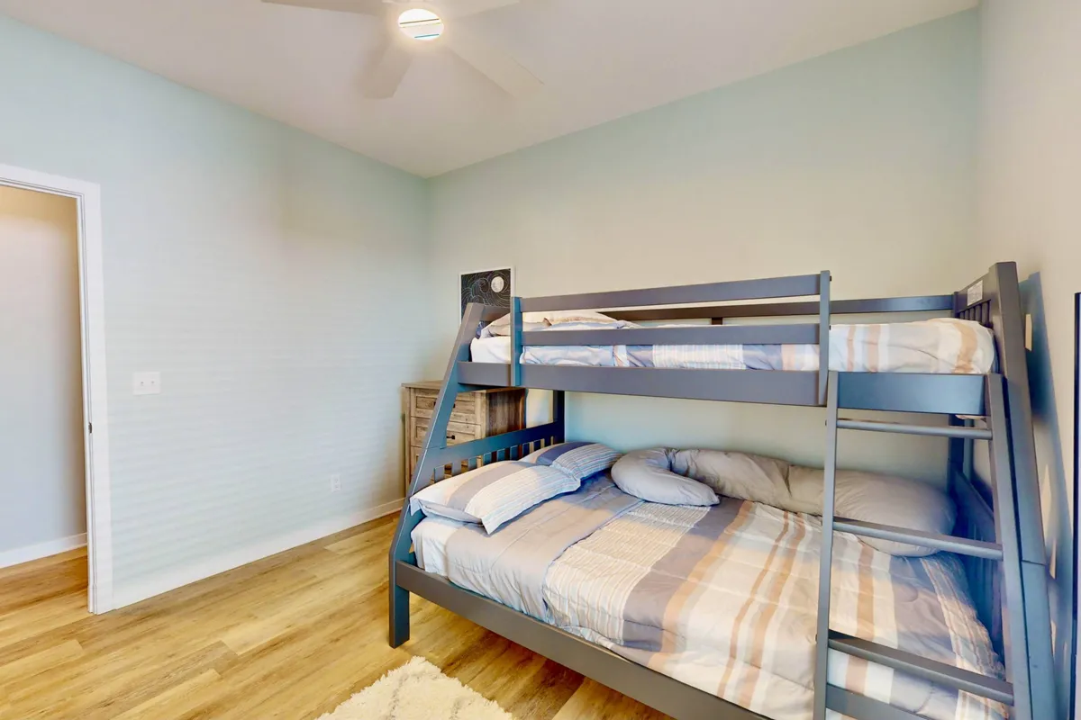 A playful and inviting bunk room featuring a twin-over-full bunk bed, a textured accent wall, and wooden flooring. The room feels cozy and perfect for children, with space for sleeping, reading, or playing games.