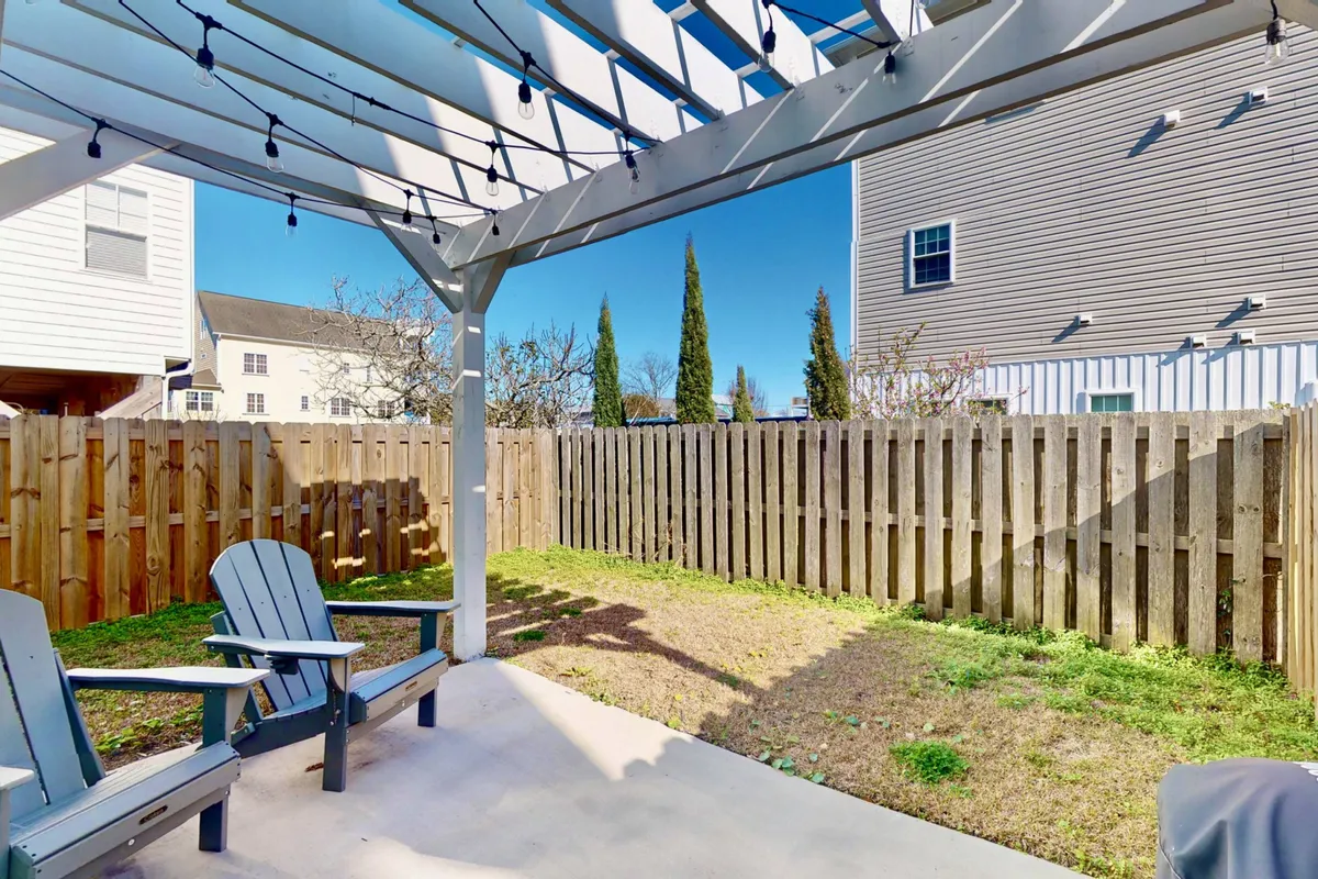 A serene, fully fenced backyard featuring a pergola, several Adirondack chairs, and a lush green lawn. The yard is clearly enclosed, making it a secure and welcoming space for dogs and children to play. The presence of seating under the pergola suggests areas for relaxation and family gatherings.
