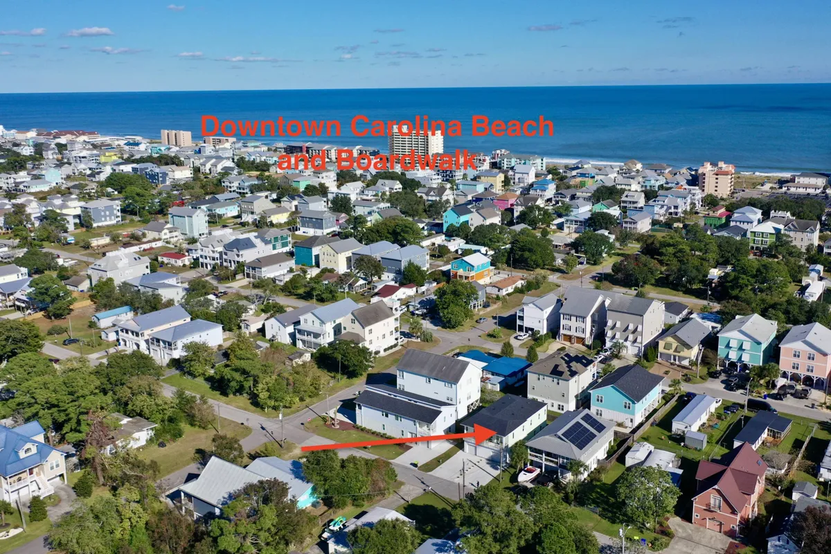 This image captures Carolina Beach with its iconic boardwalk, sandy shores, residential homes, and a sweeping ocean view. The scene is lively and inviting, hinting at bustling beach outings, boardwalk strolls, and the energy of local festivals or dining.