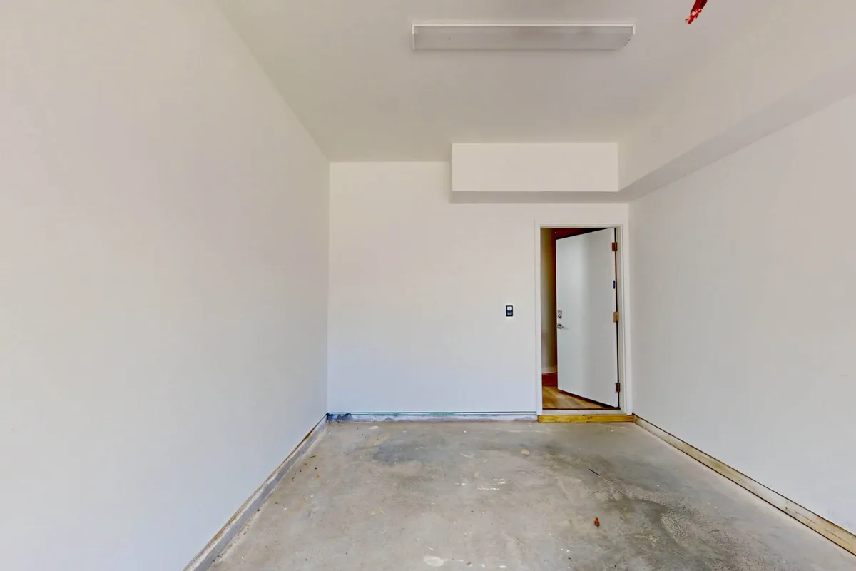 The photo shows a bare-walled, open garage or storage space with an unfinished floor and an open doorway. This utilitarian area is ready for storing outdoor gear or transforming into a personalized workshop for bikes, kayaks, or fishing equipment.