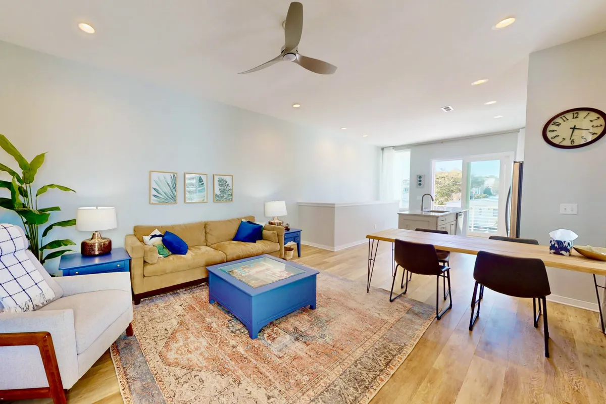This inviting living and dining space features a plush sofa, a stylish coffee table, a modern dining table perfect for family dinners, vibrant coastal artwork, and lush green plants that add a refreshing touch. The space is filled with natural light, creating a warm, welcoming atmosphere ideal for relaxing, socializing, or enjoying a quiet morning coffee together.