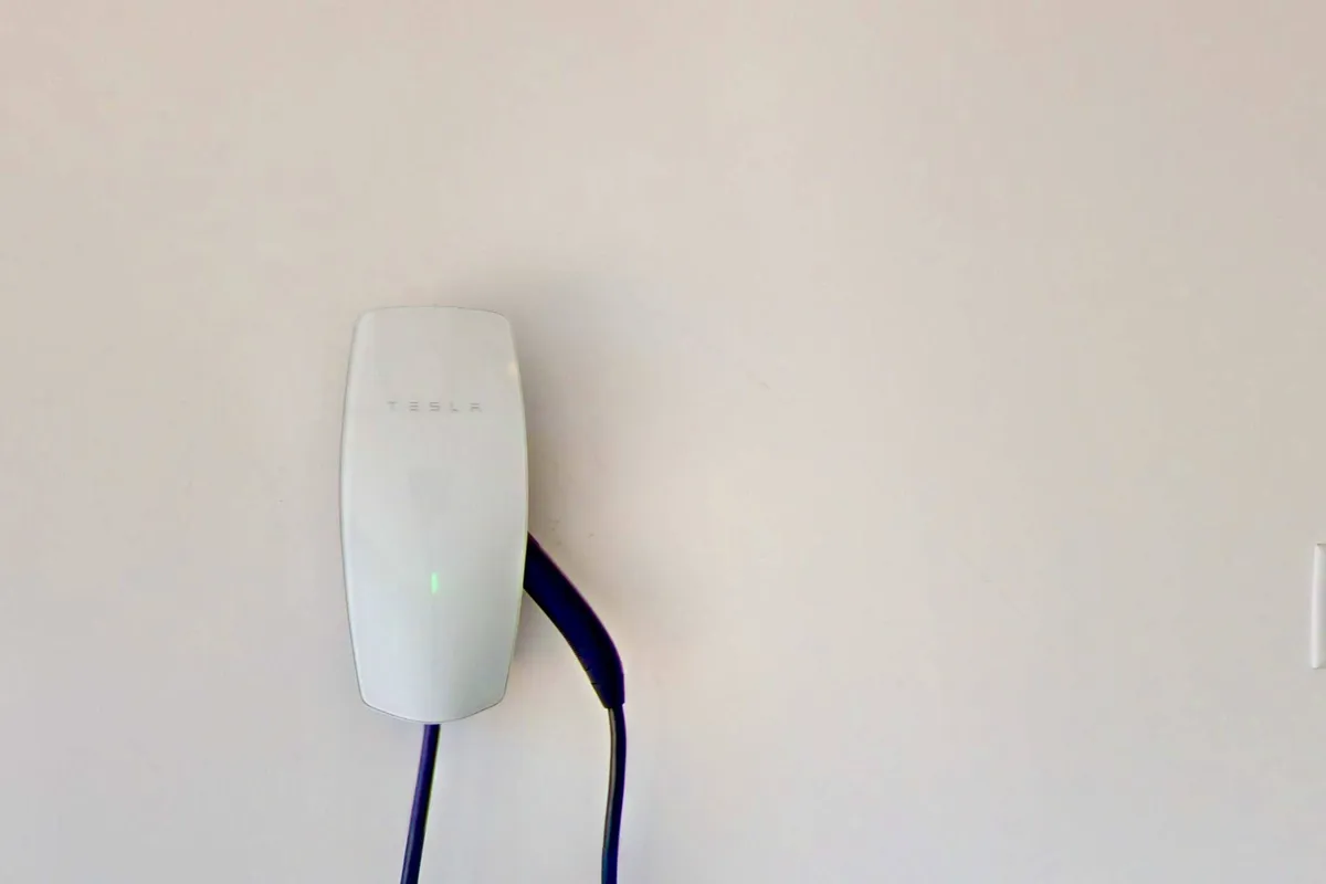 A close-up of a Tesla charger mounted on the garage wall, emphasizing the availability of electric vehicle charging facilities. The charger’s sleek, modern design hints at an eco-conscious and high-tech amenity tailored for today's travelers.