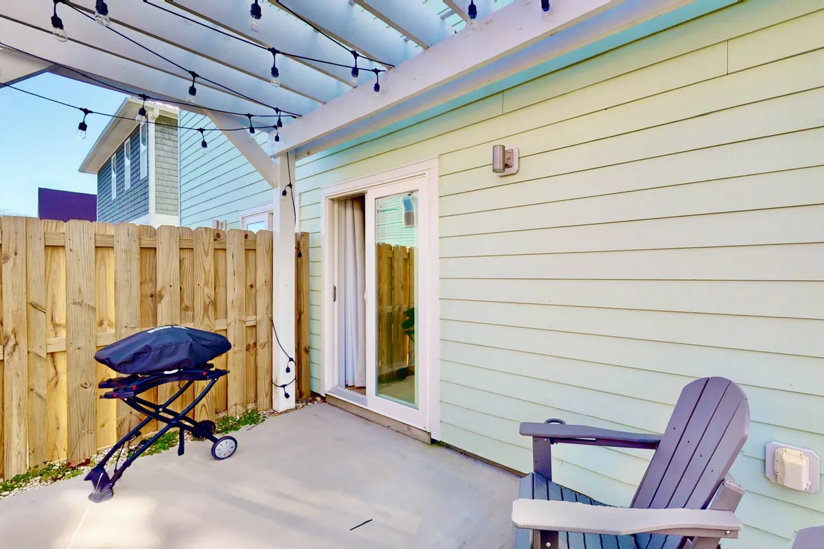 A cozy patio area with a gas grill, comfortable outdoor chairs, and decorative string lights. The setup exudes a casual, inviting atmosphere that encourages outdoor dining, barbecues, and informal gatherings as dusk approaches.